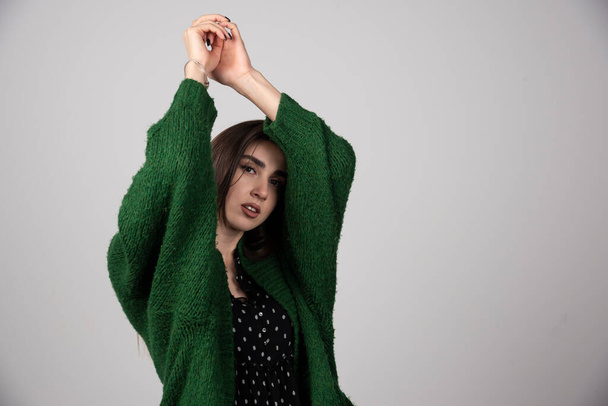 Молодая женщина в зеленом свитере позирует на сером фоне. Высокое качество фото - Фото, изображение