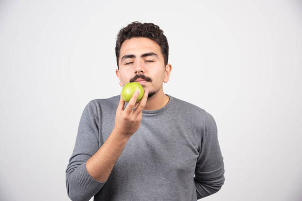 Az éhes ember szürke alapon érzi a zöld almát. Kiváló minőségű fénykép - Fotó, kép