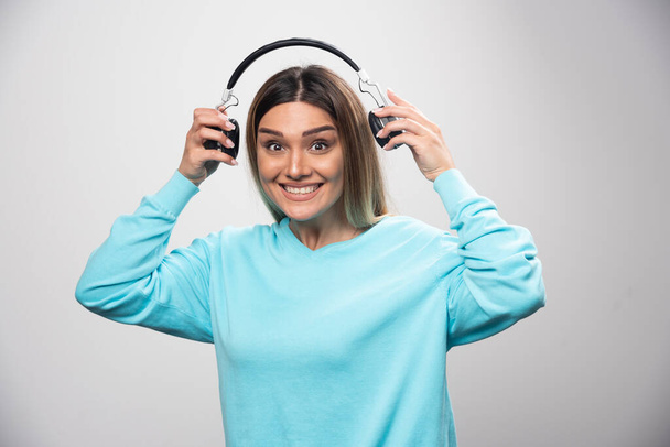 Chica rubia en sudadera azul sosteniendo auriculares y se prepara para usarlos para escuchar la música. Foto de alta calidad - Foto, imagen
