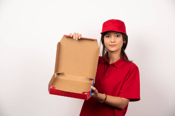 Jonge vrouw in rood uniform met lege doos pizza. Hoge kwaliteit foto - Foto, afbeelding