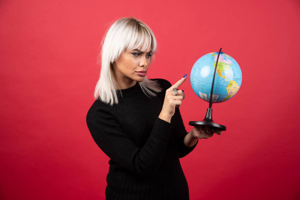 Молодая женщина показывает глобус на красном фоне. Высокое качество фото - Фото, изображение