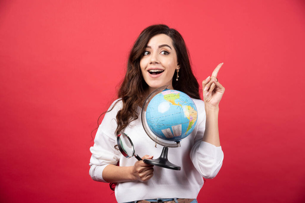 Femme heureuse posant avec globe et loupe tout en pointant vers le haut. Photo de haute qualité - Photo, image
