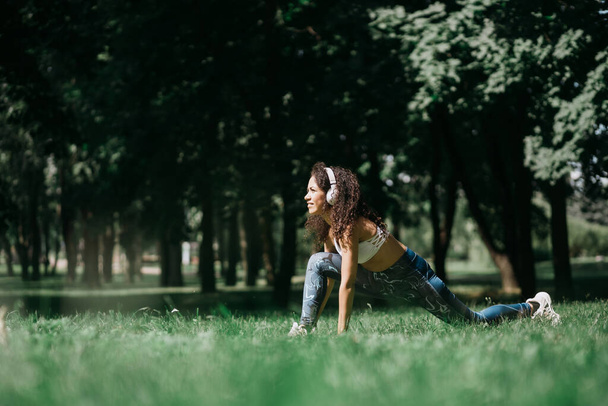 smiling woman in headphones doing stretching before jogging outdoor. - Fotoğraf, Görsel