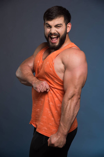 Sportman toont zijn spieren op donkerblauwe achtergrond. Hoge kwaliteit foto - Foto, afbeelding