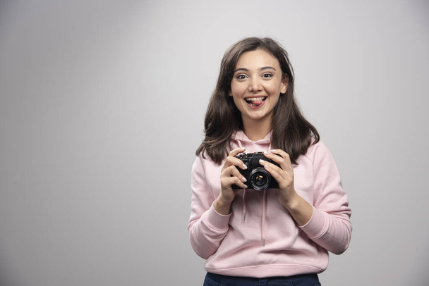Hezká mladá žena pózující s kamerou přes šedou zeď. Kvalitní fotografie - Fotografie, Obrázek
