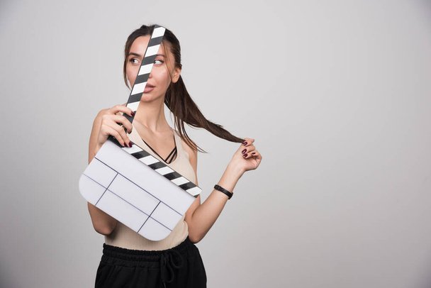 Woman in beige shirt holding clapperboard and looking aside. High quality photo - Photo, Image