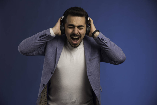 Mężczyzna w szarym garniturze, noszący słuchawki z dużą głośnością i krzykiem. Wysokiej jakości zdjęcie - Zdjęcie, obraz