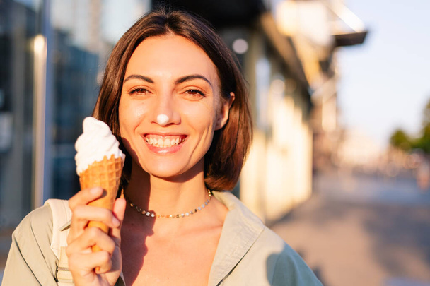 Жінка на відкритому повітрі в літній час заходу сонця маючи морозиво конус позитивний щасливий грайливий на міській вулиці
 - Фото, зображення