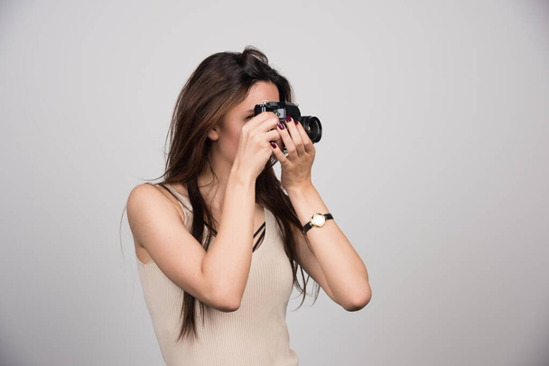 Mujer joven tomando fotos con cámara en un fondo gris. Foto de alta calidad - Foto, imagen