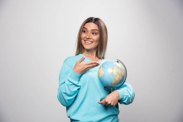 Blonde girl in blue sweatshirt holding a globe, guessing location and having fun. High quality photo - Фото, зображення