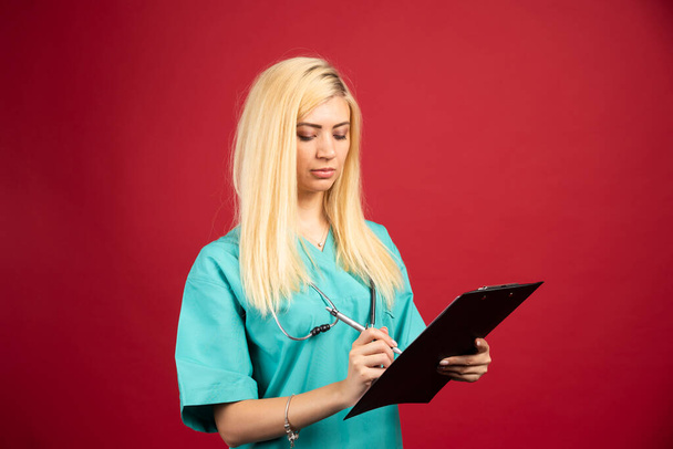 Serious nurse writing notes on her clipboard. High quality photo - Foto, imagen