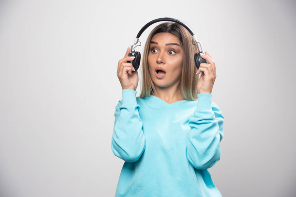 Blonde girl in blue sweatshirt taking out the headphones to hear the people around. High quality photo - Фото, зображення