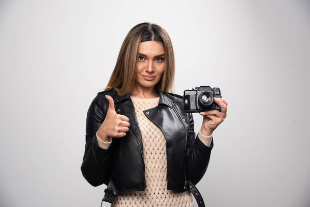 Jeune femme veste en cuir noir prenant des photos avec appareil photo d'une manière positive et souriante. Photo de haute qualité - Photo, image