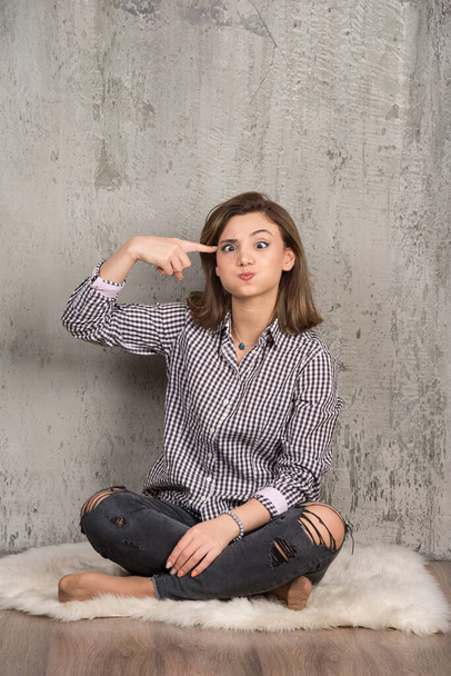 Portrait of a young pretty girl in plaid shirt pointing at head . High quality photo - Φωτογραφία, εικόνα