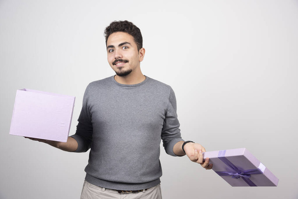 Uśmiechnięty mężczyzna z otwartym fioletowym pudełkiem na białej ścianie. Wysokiej jakości zdjęcie - Zdjęcie, obraz