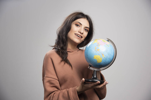 Brunette woman holding globe on gray background. High quality photo - Foto, immagini
