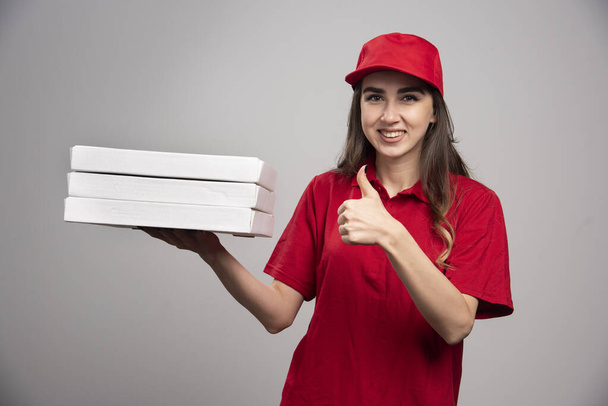 Női futár pizzás dobozokkal és feltartott hüvelykujjakkal. Kiváló minőségű fénykép - Fotó, kép