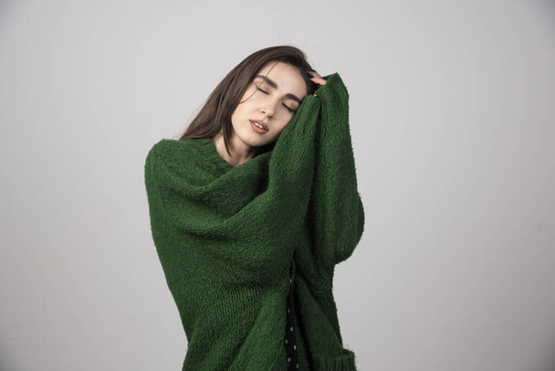 Egy fiatal nő zöld pulóverben szürke háttéren alszik. Kiváló minőségű fénykép - Fotó, kép