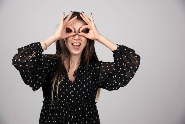 Pretty girl with smile holding fingers near eyes like glasses. High quality photo - Photo, Image