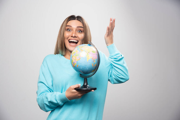 Blonde girl in blue sweatshirt holding a globe, guessing location and having fun. High quality photo - Photo, image