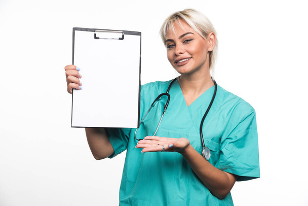 Doctora sonriente sosteniendo un portapapeles apuntando con la mano sobre fondo blanco. Foto de alta calidad - Foto, imagen