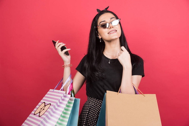 Young woman with glasses holding her bags and phone on red background - Photo, image
