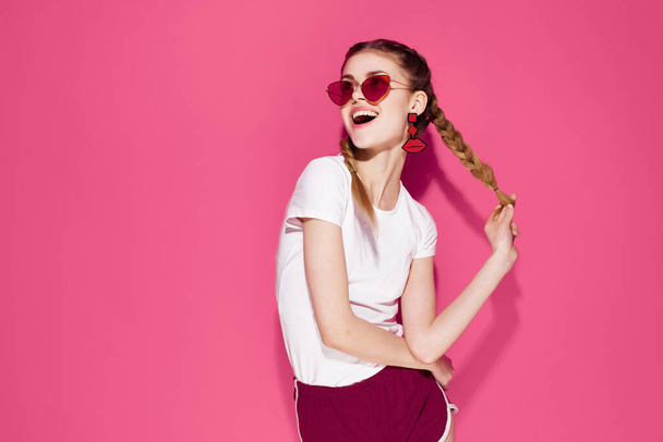 mooie vrouw dragen zonnebril glamour vlechten lifestyle mode roze achtergrond - Foto, afbeelding