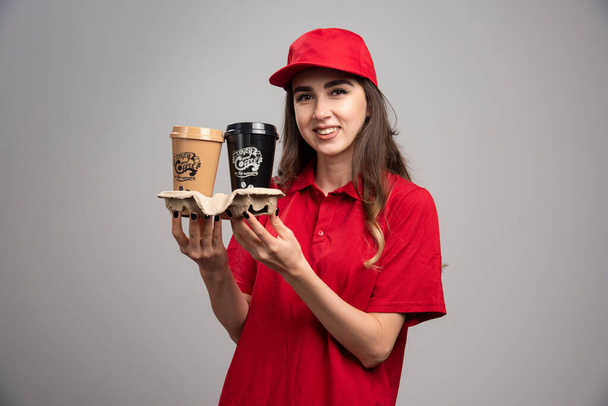Belle femme de livraison en uniforme rouge tenant des tasses à café. Photo de haute qualité - Photo, image