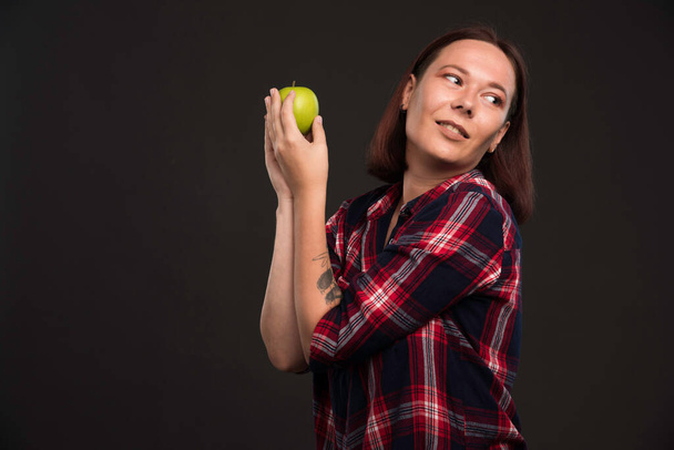 Θηλυκό μοντέλο σε φθινοπωρινή συλλογή ρούχα κρατώντας ένα πράσινο μήλο και απολαμβάνοντας το. Υψηλής ποιότητας φωτογραφία - Φωτογραφία, εικόνα