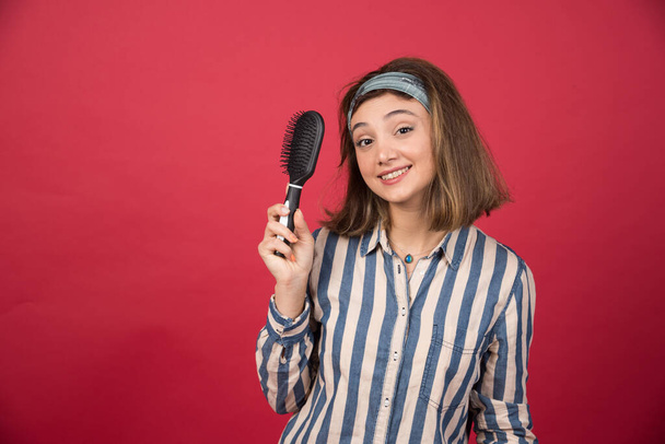Young girl with tangled hair showing comb on red background. High quality photo - Photo, Image