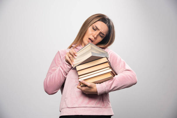 Dziewczyna w różowej koszuli, trzymająca zapas książek, otwierająca jedną na górze i czytająca ją. Wysokiej jakości zdjęcie - Zdjęcie, obraz