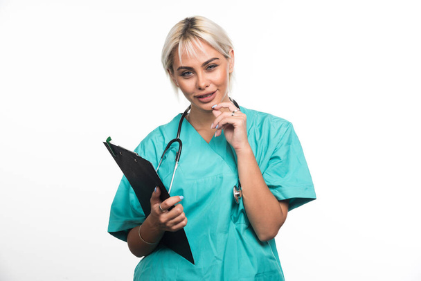 Medico femminile che tiene appunti mentre pensa su sfondo bianco. Foto di alta qualità - Foto, immagini
