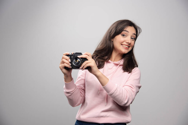 Mujer joven y bonita posando con cámara sobre una pared gris. Foto de alta calidad - Foto, imagen