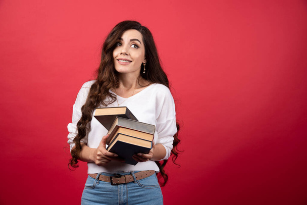 Молодая женщина-модель держит книги на красном фоне. Высокое качество фото - Фото, изображение