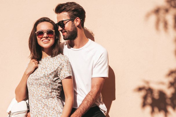 Portrait of smiling beautiful woman and her handsome boyfriend. Woman in casual summer clothes. Happy cheerful family. Female having fun. Couple posing in the street near wall in sunglasses - Foto, afbeelding