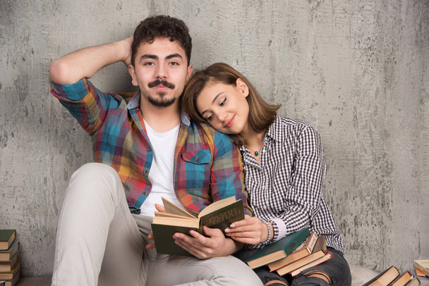 Zdjęcie młodej uśmiechniętej pary siedzącej na podłodze z książkami. Wysokiej jakości zdjęcie - Zdjęcie, obraz