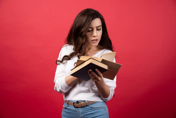 Brunette vrouw leest boek over rode achtergrond. Hoge kwaliteit foto - Foto, afbeelding
