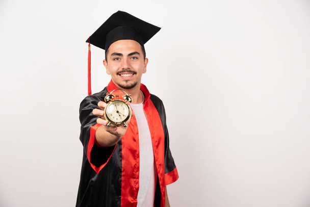 Mladý absolvent drží hodiny na bílém pozadí. Kvalitní fotografie - Fotografie, Obrázek