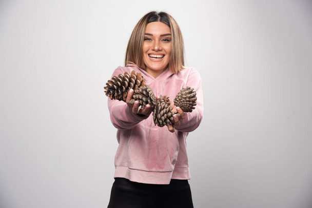 Blonde lady in pink sweatshirt offering oak tree cones with happiness. High quality photo - Photo, Image