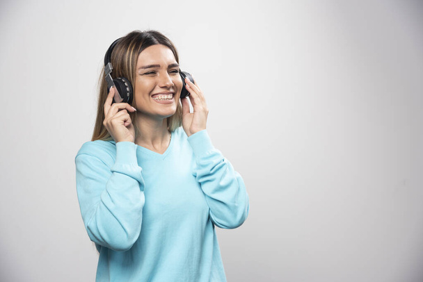 Blonde girl in blue sweatshirt wearing headphones, enjoying the music and having fun. High quality photo - Photo, Image