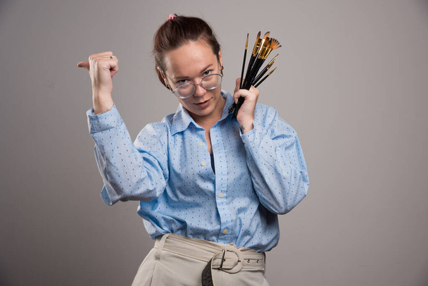 Žena umělkyně drží štětce na šedém pozadí. Kvalitní fotografie - Fotografie, Obrázek