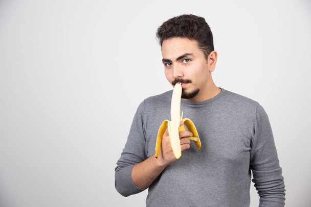A young man eating a banana over a white wall. High quality photo - Foto, Imagen