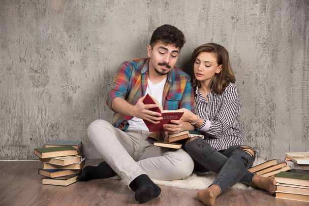 Una pareja encantadora leyendo un libro interesante mientras está sentada en el suelo. Foto de alta calidad - Foto, imagen