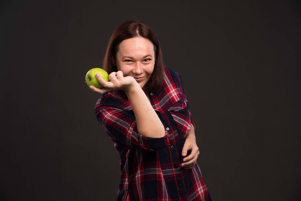 Θηλυκό μοντέλο σε φθινοπωρινή συλλογή ρούχα κρατώντας ένα πράσινο μήλο και διασκεδάζοντας. Υψηλής ποιότητας φωτογραφία - Φωτογραφία, εικόνα