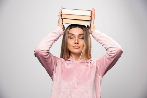Chica con una camisa rosa sosteniendo sus libros sobre su cabeza. Foto de alta calidad - Foto, Imagen