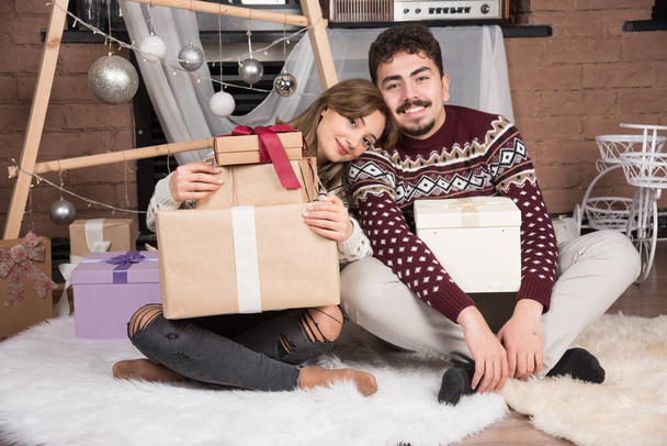 Giovane coppia seduta con regali di Natale vicino palle d'argento festive. Foto di alta qualità - Foto, immagini