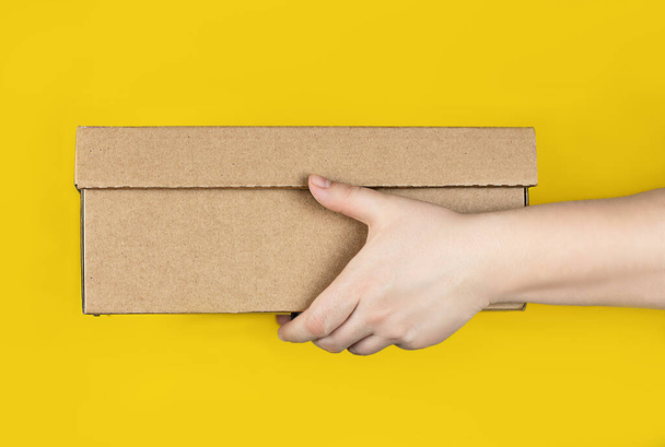 Large cardboard box in hands on a trendy yellow background. Horizontal photo. Concept - delivery of orders to your home by courier, receipt of parcels, safe distance - Foto, Imagem