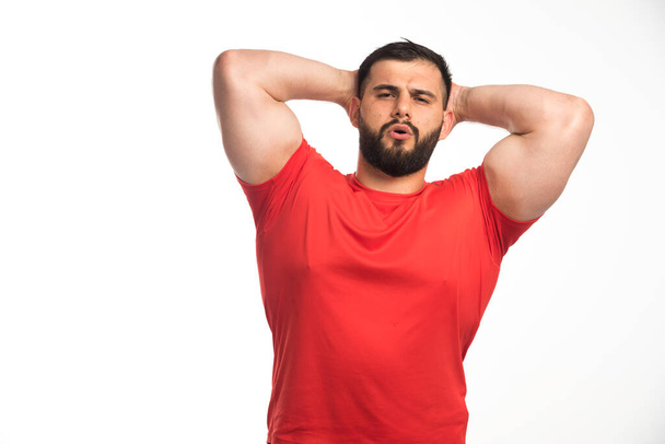 Sportive man in red shirt demonstrating his muscles and put hands to his head. High quality photo - Foto, imagen