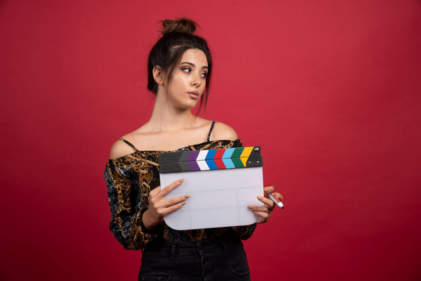 Brunette girl holding a blank clapper board for film production on red background. High quality photo - Fotó, kép