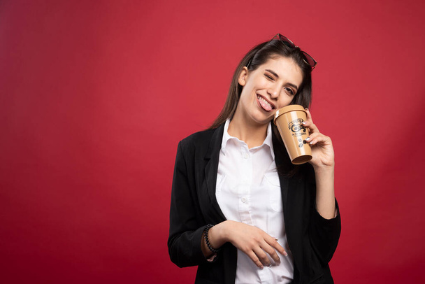 Młoda bizneswoman trzymająca kawę na czerwonym tle. Wysokiej jakości zdjęcie - Zdjęcie, obraz